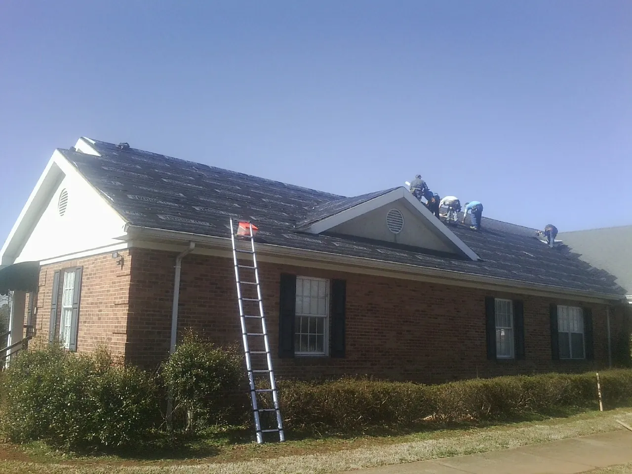 Crew tearing shingles off a brick ranch roof with a ladder set — Emergency Roof Repair work by our crew in Lynnfield