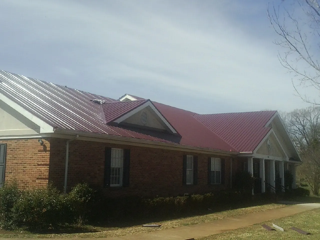 Red metal roof with gabled entries on a long brick building, from a Hail Damage Roof Repair job in Lynnfield