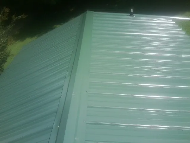 New green metal panels meeting at the ridge of a roof — Flat Roof Repair work by our crew in Lynnfield
