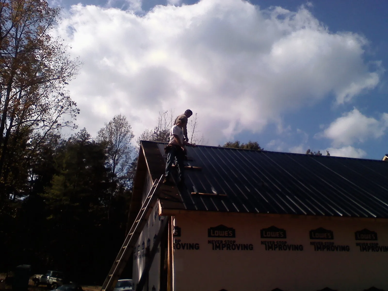 Roofer fastening dark metal panels high against a cloudy sky, from a Roof Inspection job in Lynnfield