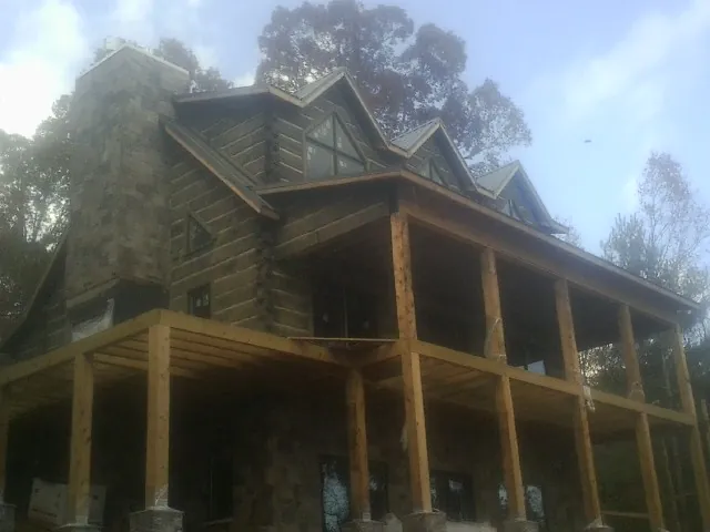 Stone chimney and dormers on a large log home with a timber porch in Lynnfield