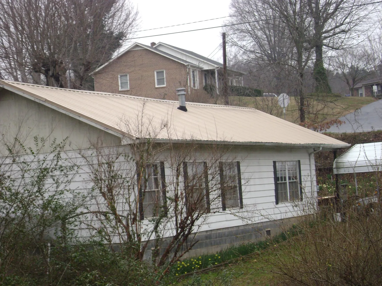 Tan metal roof on a white sided house set into a hillside — Commercial Roofing by Roofing Brothers in Lynnfield